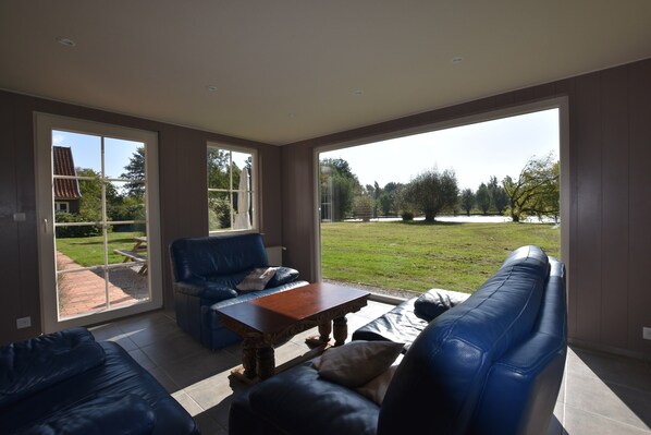 A spacious living area with a large sliding glass door leading to a backyard, a blue leather sofa, and a wooden coffee table. - Holiday Home in Saint-omer Near Lake & Forest (Saint-Omer)