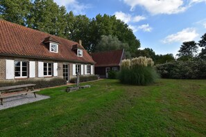 A brick building with a red-tiled roof, a wooden bench, and a grassy yard. - Holiday Home in Saint-omer Near Lake & Forest (Saint-Omer)