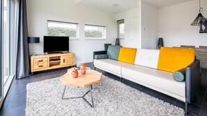 A modern living room with a white sofa, a wooden coffee table, and a flat-screen TV on a wooden cabinet. - Modern Villa with Large Garden by the Water with Hot Tub & Infrared Sauna (Zeewolde)