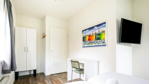 A hotel room with a bed, a desk, a chair, a television, and a painting on the wall. - Modern Villa with Large Garden by the Water with Hot Tub & Infrared Sauna (Zeewolde)