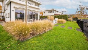 A modern two-story house with a patio area, a well-maintained lawn, and a black fence. - Modern Villa with Large Garden by the Water with Hot Tub & Infrared Sauna (Zeewolde)