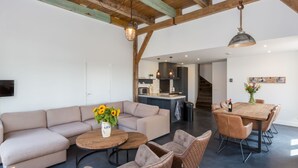 Een ruime woonkamer met een grote bank, twee ronde salontafels en een eettafel met stoelen.