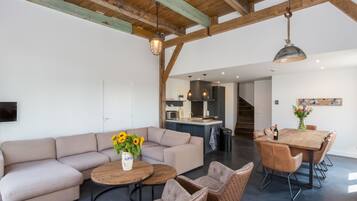 Een ruime woonkamer met een grote bank, twee ronde salontafels en een eettafel met stoelen.