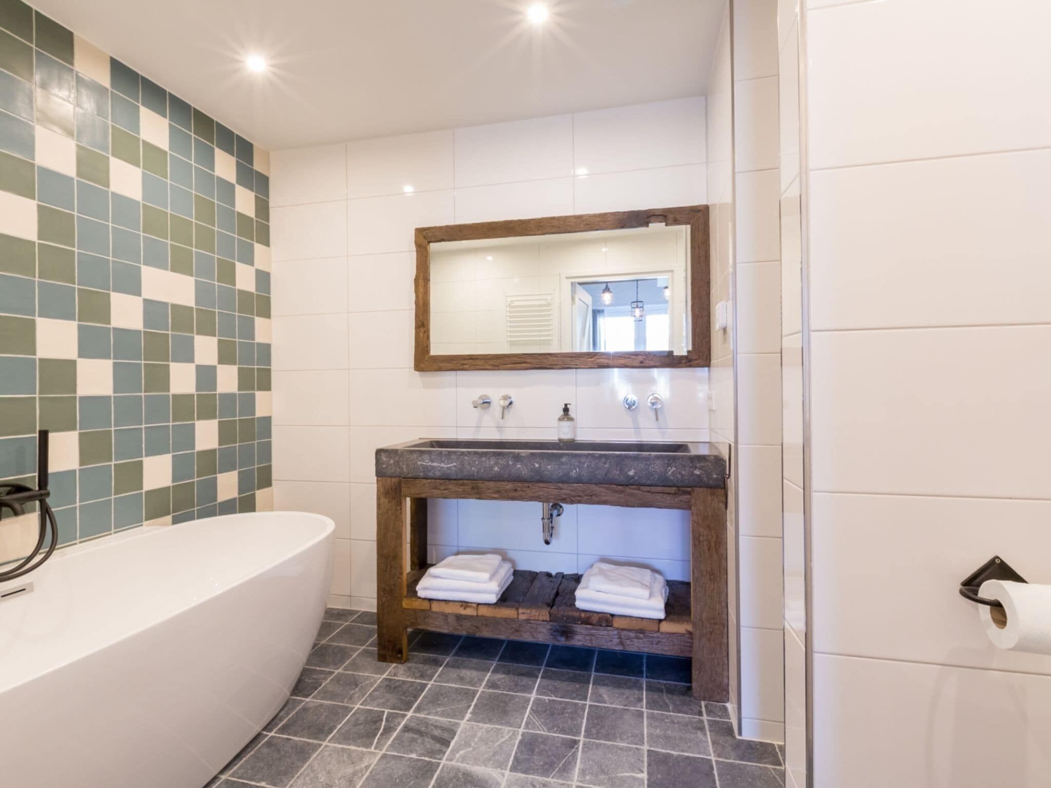 A bathroom with a bathtub, a sink with a wooden vanity, and a mirror above the sink.
