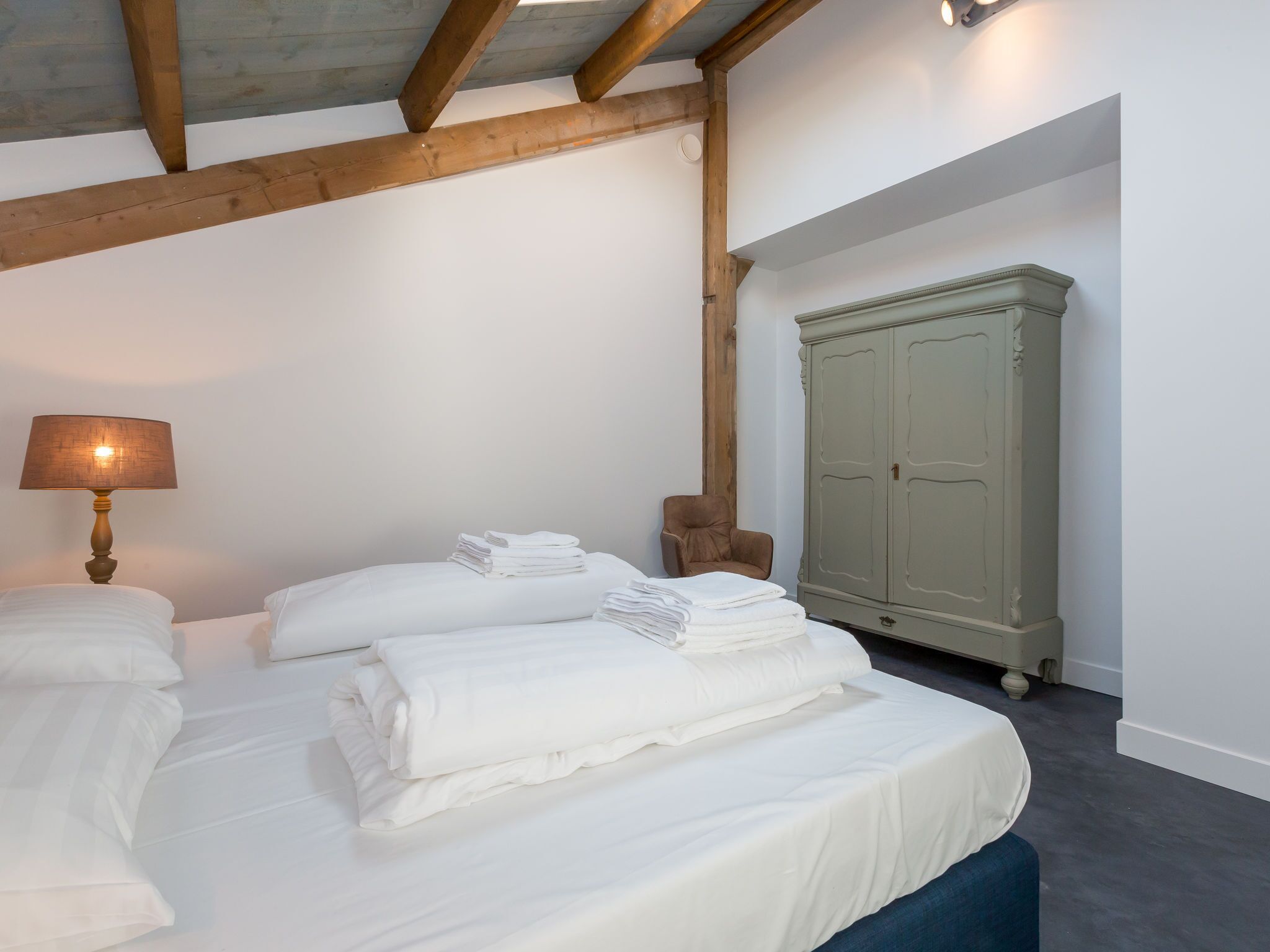 A bedroom with two beds, a lamp, a wardrobe, and a chair.