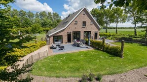 Een huis met een schuin dak, grote ramen en een terras met tuinmeubilair.