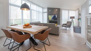 Ein modernes Wohnzimmer mit einem Holzesstisch, braunen Ledersesseln, einem grauen Sofa und einem flachbildfernseher an der Wand.