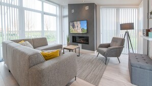 Ein modernes Wohnzimmer mit grauem Sofa, einem kleinen Tisch, einem an einer strukturierten Wand befestigten Fernseher und einer Stehlampe.