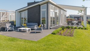 Ein modernes Haus mit Terrasse, einem grauen Sofa und einem weißen Tisch.