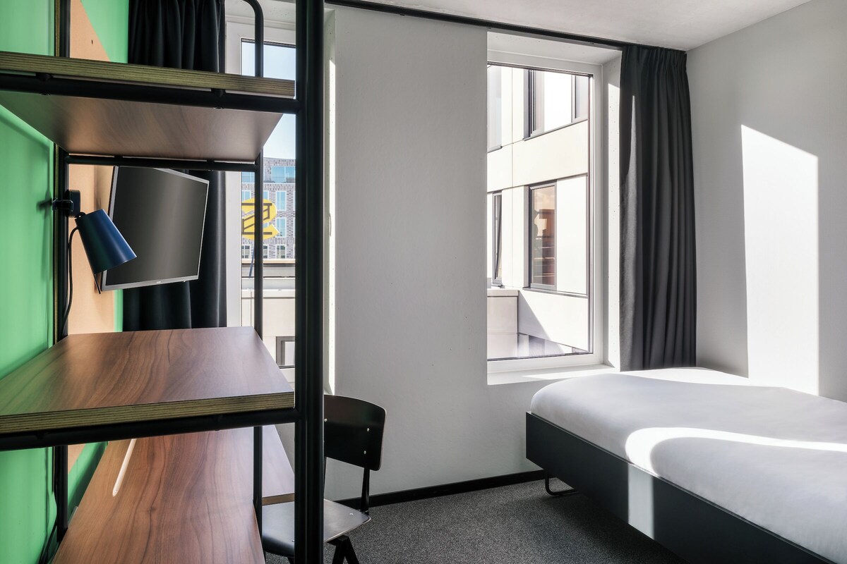 Habitación de hotel con literas, un escritorio con silla, un televisor de pantalla plana y una ventana con cortinas.