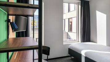 Een hotelkamer met een stapelbed, een bureau met stoel, een flatscreen televisie en een raam met gordijnen.