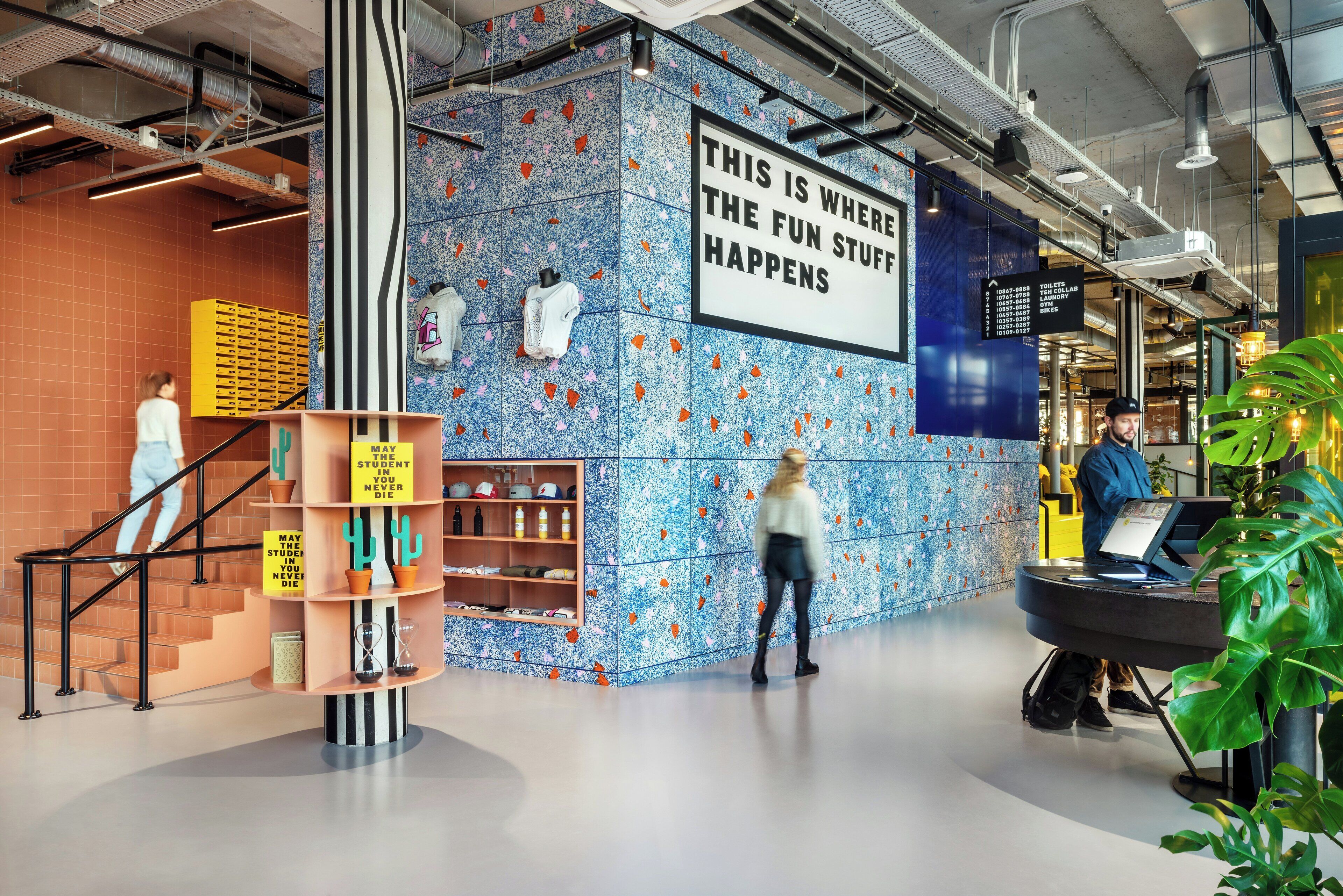 Een modern interieur met een blauwe patroonwand, een bord met de tekst 'THIS IS WHERE THE FUN STUFF HAPPENS' en een trap met gele opbergkisten.