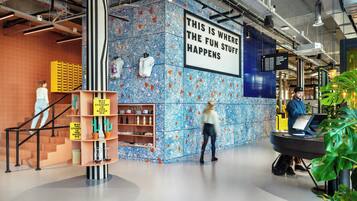 Een modern interieur met een blauwe patroonwand, een bord met de tekst 'THIS IS WHERE THE FUN STUFF HAPPENS' en een trap met gele opbergkisten.