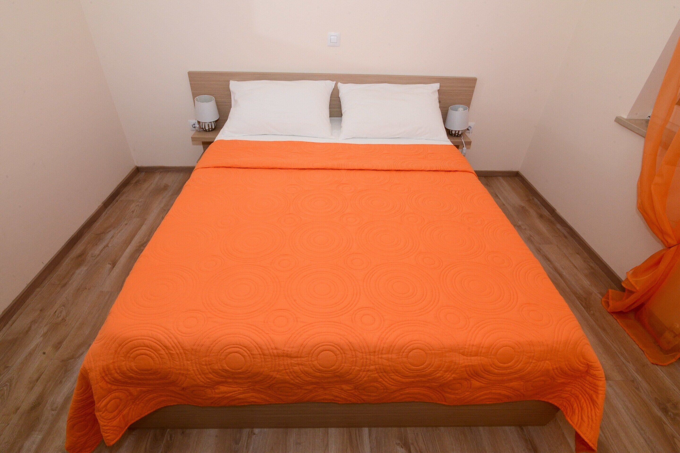 Un lit avec une couvre-lit orange, deux oreillers blancs et deux lampes de chevet.