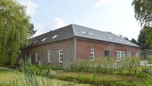A brick building with a sloped roof and skylights, surrounded by greenery and a small pond. - Swolgen Estate With Sauna (Swolgen)