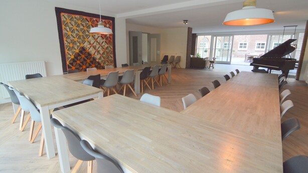 A spacious dining area with long wooden tables and modern chairs, a large decorative wall, and a grand piano in the background. - Swolgen Estate With Sauna (Swolgen)