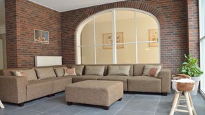 A living room with a sectional sofa, an ottoman, a potted plant, and a large arched window. - Swolgen Estate With Sauna (Swolgen)