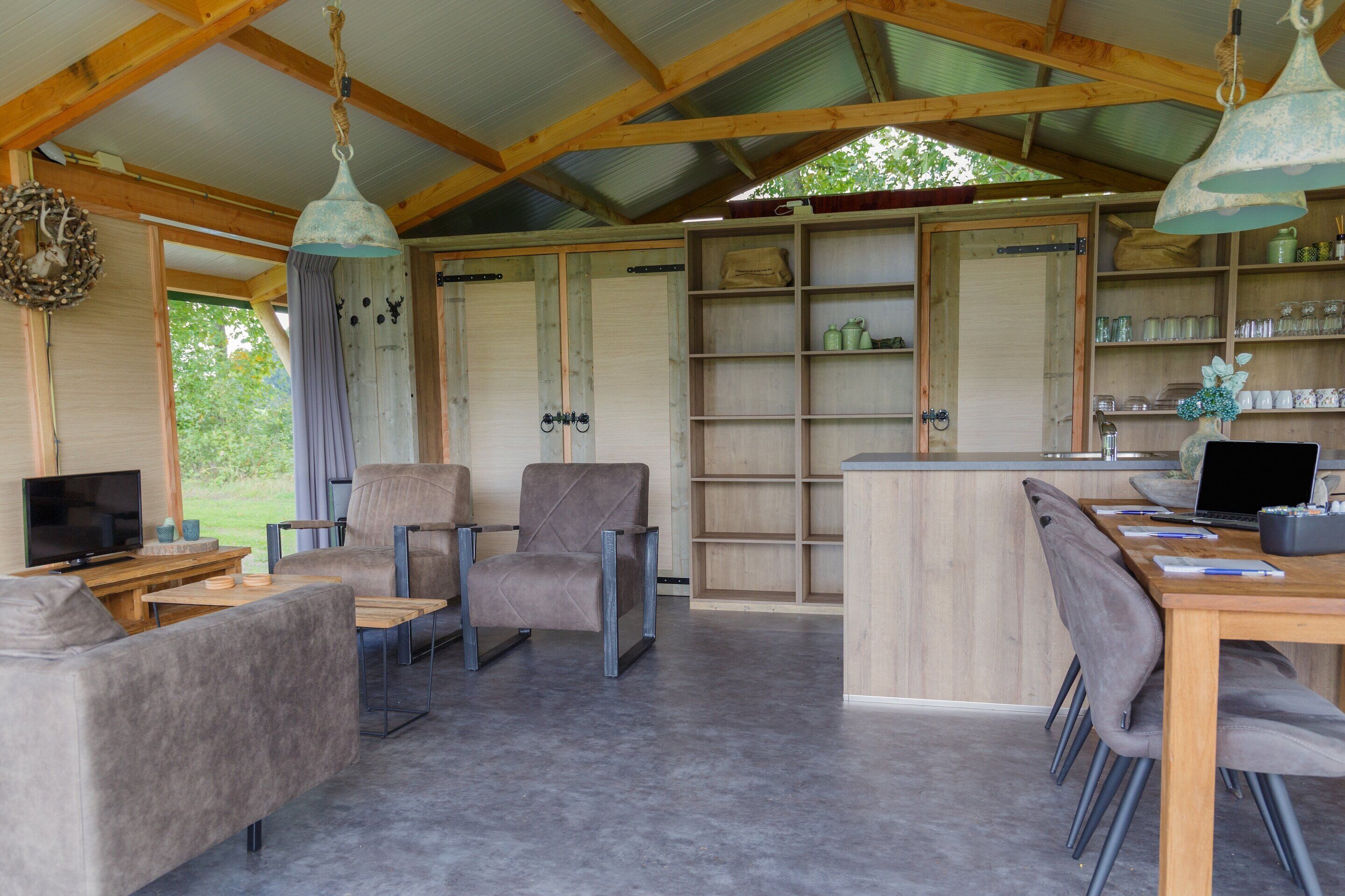 A spacious living area with a sofa, chairs, a wooden table, a television, and a kitchen area with a bar.