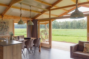 A spacious room with a wooden ceiling, a dining area with chairs and a table, and a large window with a view of a green field.