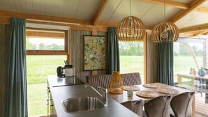 A modern kitchen with a large island, wooden beams, and a view of the outdoors. - Tent Lodge With Dishwasher in Twente (Haaksbergen)