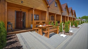 A row of wooden cabins with a covered patio area, benches, and small trees. - Bungalow in Mielenko Baltic Coast With Garden (Mielno)