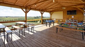 A covered outdoor area with wooden tables and benches, a fire pit, and a view of the countryside. - Bungalow in Mielenko Baltic Coast With Garden (Mielno)