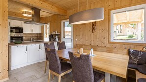 A wooden interior with a dining table, chairs, a kitchen area, and a large window. - Attractive Chalet With Whirlpool (Sankt Georgen am Kreischberg)