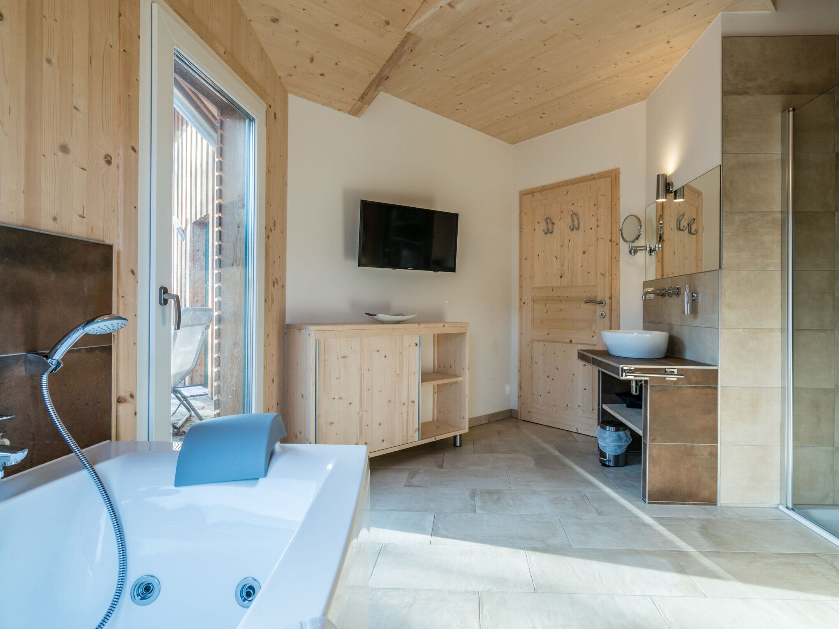 A modern bathroom with a large bathtub, wooden cabinets, a television, and a shower area.