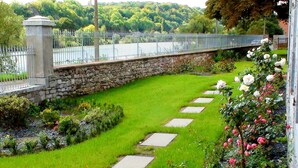 Un jardín con un muro de piedra, un camino empedrado y un puente sobre un estanque.