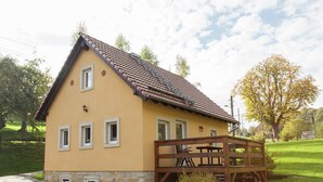 A yellow building with a tiled roof and a wooden deck with tables and chairs. - Sachsischer Wald Ruckzug (Hohnstein)