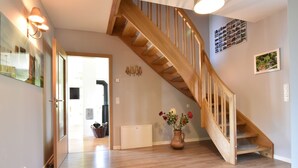 A spacious hallway with a wooden staircase, a vase with flowers, and a door leading to another room. - Ferienhaus vor den Toren der Insel Poel (Hornstorf)