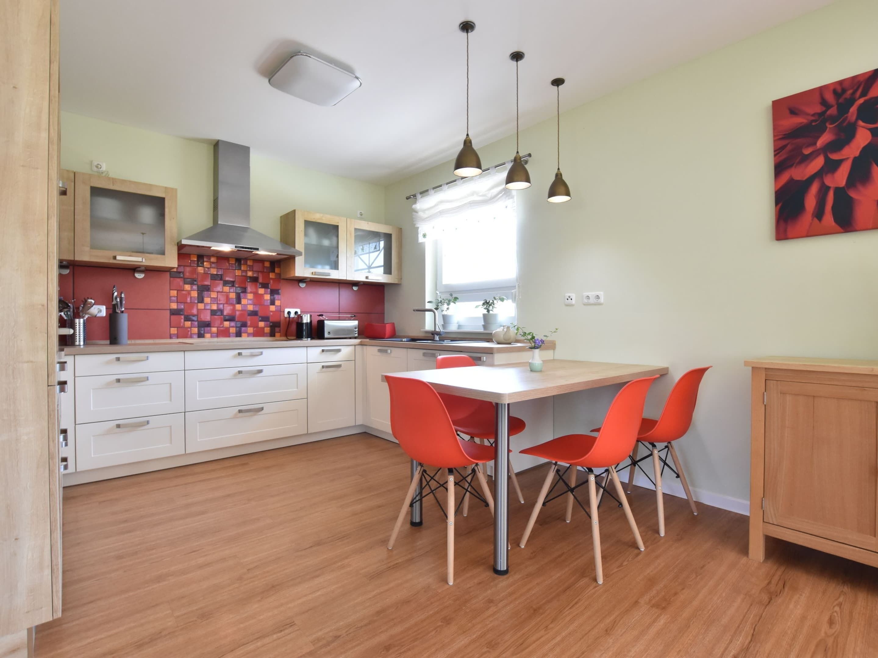 Une cuisine moderne avec des meubles en bois, un pare-feu en carrelage et un coin repas avec des chaises orange.