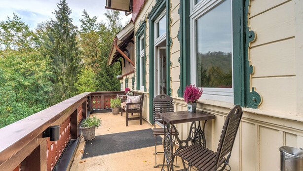 A balcony with a wooden railing, a table, two chairs, and a potted plant. - Gruppenhaus im Harz (Bad Harzburg)