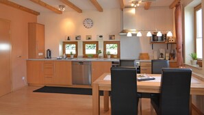 A modern kitchen with wooden beams, a stainless steel dishwasher, and a dining area with a table and chairs.