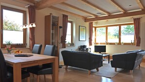 A spacious living area with a wooden dining table, black sofas, and a TV.