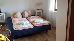 Quarto com cama, almofadas, escrivaninha, luminária e um quadro na parede.