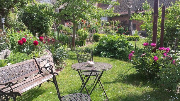 Um jardim com um banco de madeira, duas mesas de metal e diversas plantas e flores.