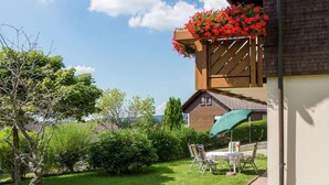 A backyard with a wooden deck, a table with chairs, and a green umbrella. - Apartment in Neukirch With Terrace (Furtwangen)
