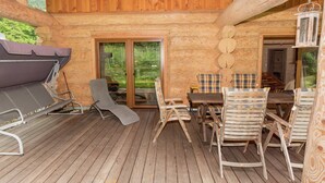 Eine Holzhütte mit Terrasse, Grill und Tisch mit Stühlen.