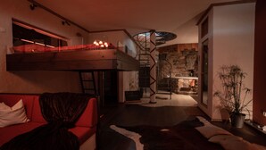 A modern interior with a loft bed, a red sofa, a cowhide rug, and a staircase leading to a kitchen area.