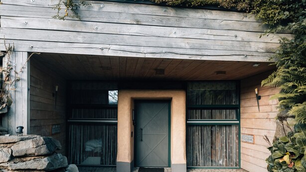 A rustic building with a stone wall entrance, a wooden door, and a cobblestone pathway.