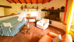 Uma sala de estar acolhedora com um sofá listrado, uma poltrona branca e uma mesa de centro de madeira. Há uma lareira com uma prateleira acima, decorada com objetos.