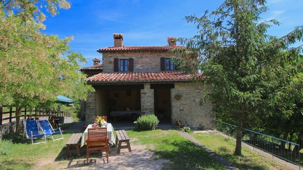 Una casa de piedra con techo de tejas, un patio con mesa y sillas, y un jardín.