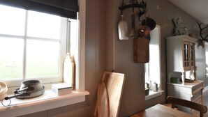 Une cuisine avec une fenêtre, une planche à découper en bois, un meuble blanc et un luminaire suspendu.