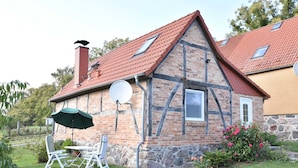 Ett traditionellt hus med korsvirkesfasad, ett sluttande tak täckt med röda tegelpannor, en satellitmottagare och en grund av sten.