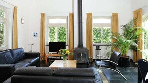 Ein Wohnzimmer mit Kamin in Schwarz, einer Couch, einem Couchtisch mit Blumen und einem Fernseher.