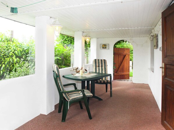 A covered patio area with a table and chairs, a wooden door, and a view of greenery outside. - Coastal Stay, Kuhlungsborn (Kuehlungsborn)