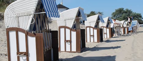 Beach huts with striped awnings, wooden frames, and a sandy beach in the background.