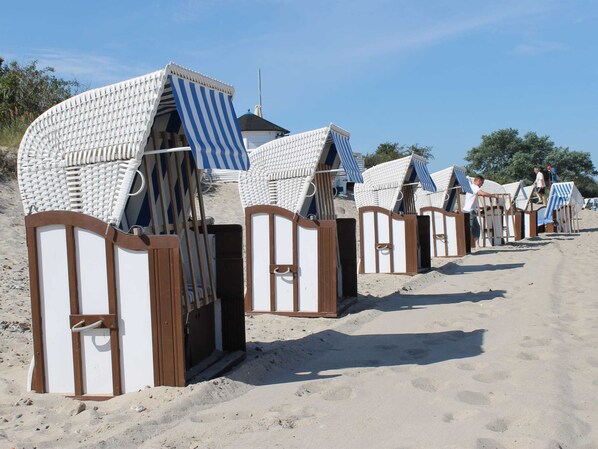 Beach huts with striped awnings, wooden frames, and a sandy beach in the background.