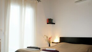 Una cama bien hecha con un cabecero, una mesita de noche con una lámpara y un pequeño estante con libros.